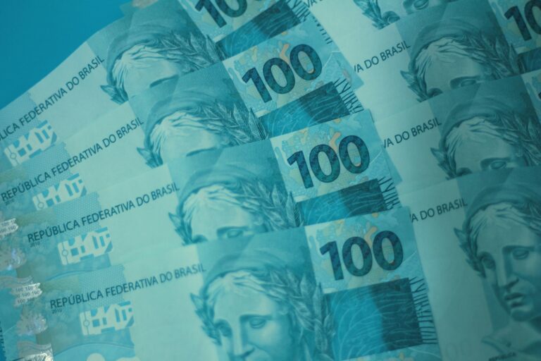 Cédulas de 100 reais empilhadas, representando dinheiro físico e o sistema bancário brasileiro.
