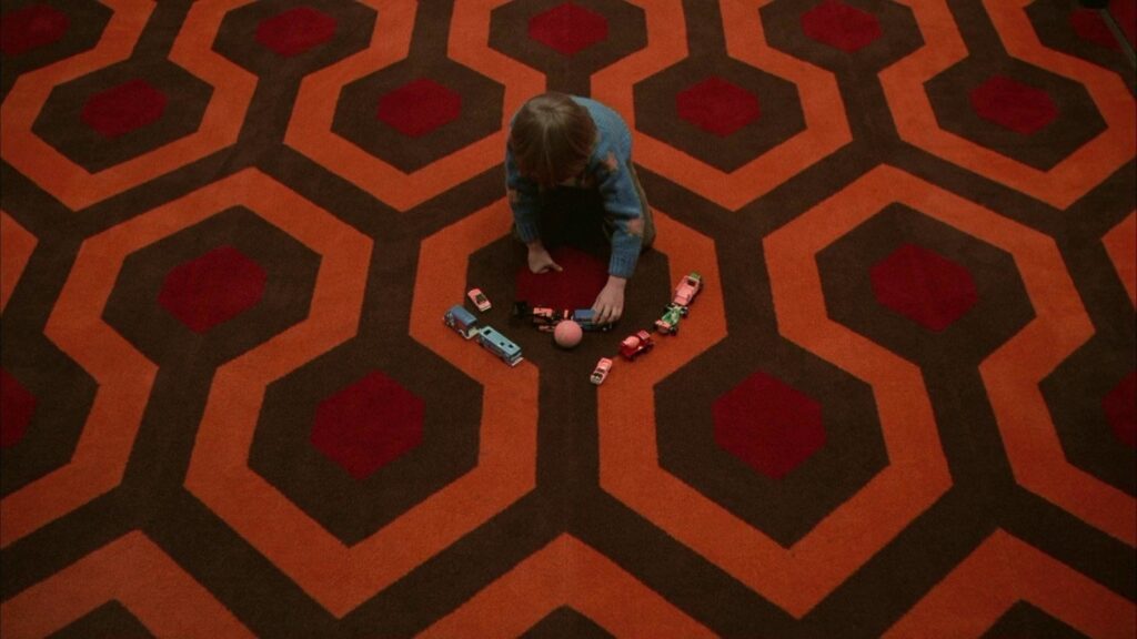 Danny brincando com carrinhos no tapete do hotel em O Iluminado