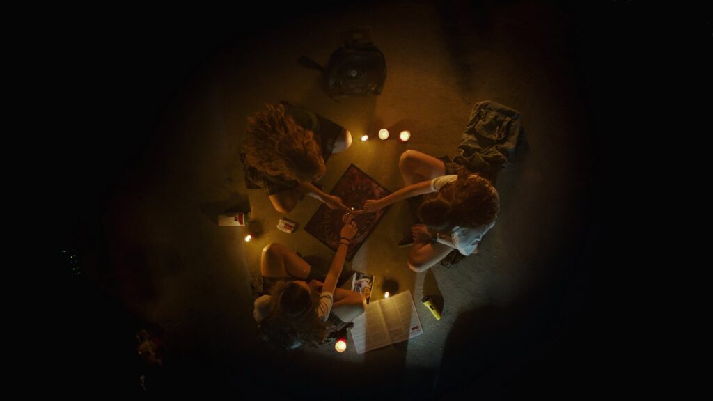 Mesa de ouija iluminada por velas em cena de Verónica